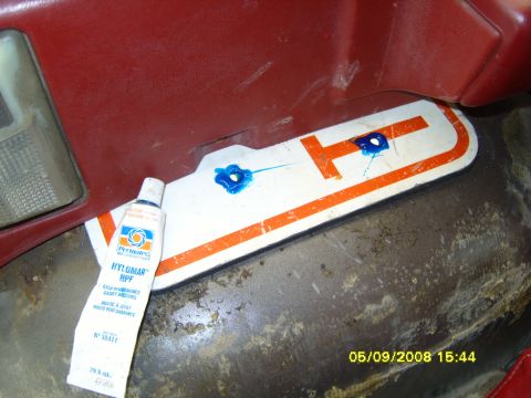 1989 Ford Bronco - A white and orange plastic trim panel rests on a bare metal surface with two dabs of blue silicone sealant applied to its mounting holes, b…