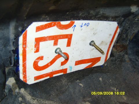 1989 Ford Bronco - A piece of white and orange aluminum road sign cut into a trim panel and test-fitted over rusty sheet metal, with two bolts poked through t…