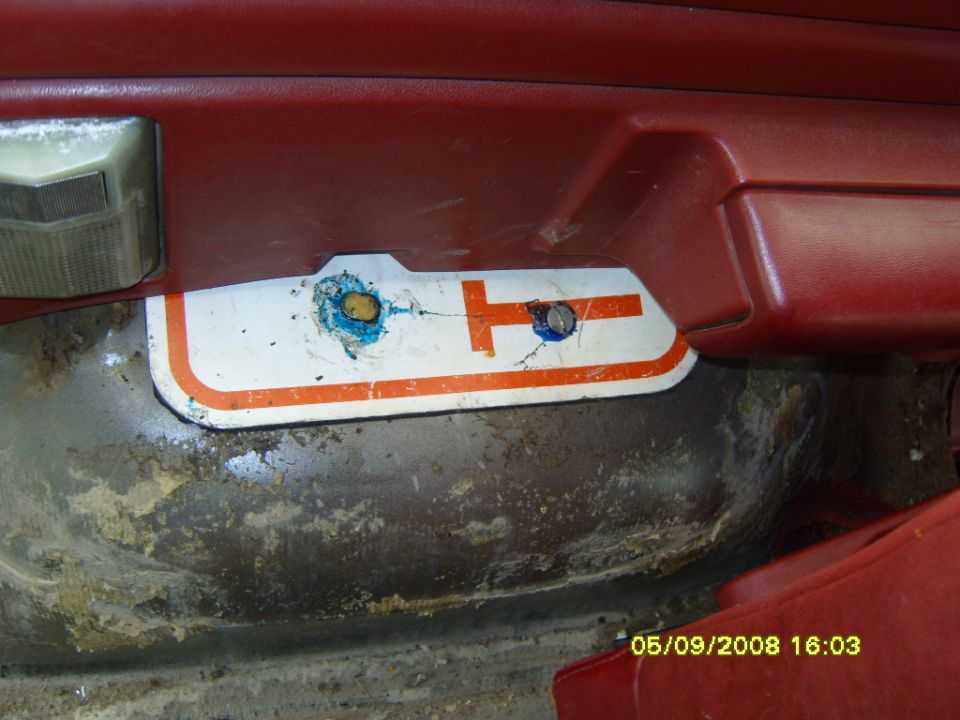 Red interior door panel with lower trim removed showing rusty bare metal and a placard