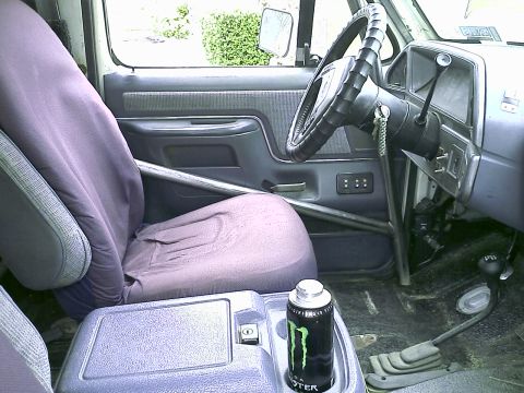1990 Ford Bronco - Interior view of a 1990 Ford Bronco showing the driver's seat, dashboard, steering wheel, and floor shifter. A can of Monster Energy drink…