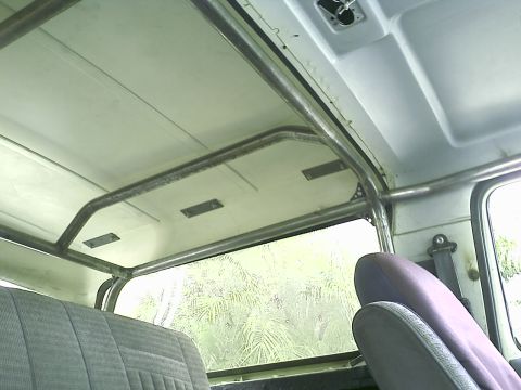 1990 Ford Bronco - Interior of a full-size SUV looking up and rearward at a bare-metal welded roll bar hoop running across the white painted headliner and inn…
