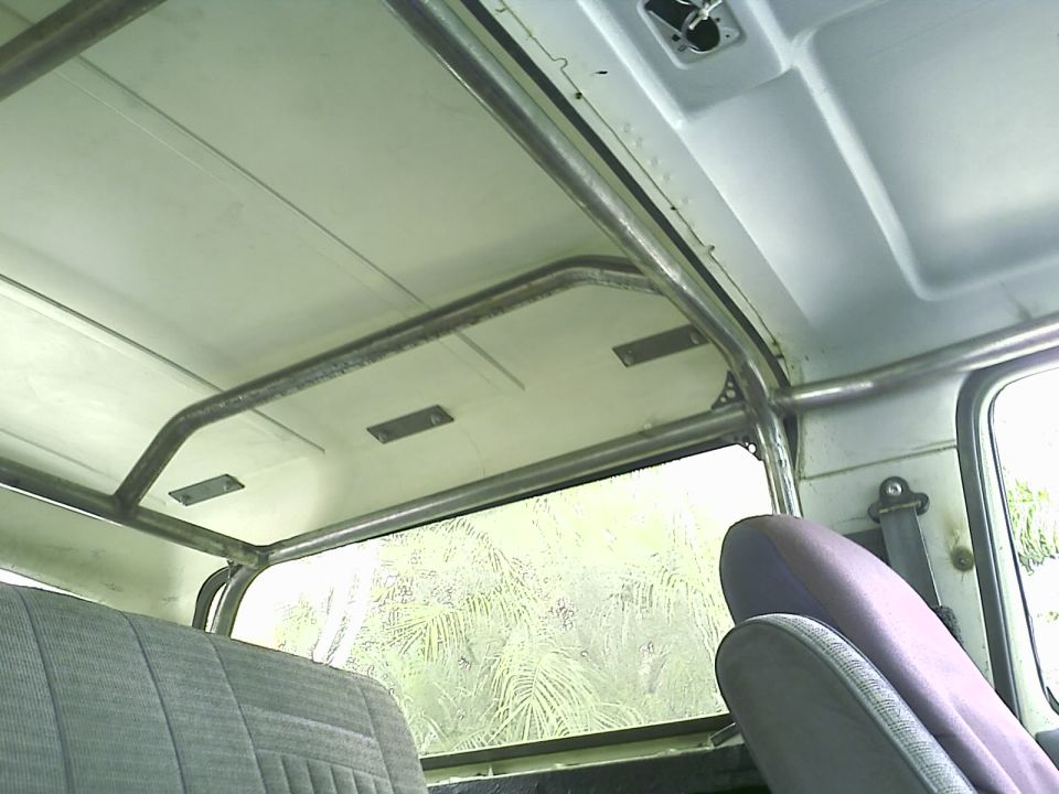 Bare metal roll bar across the white painted roof inside an SUV with gray cloth seats