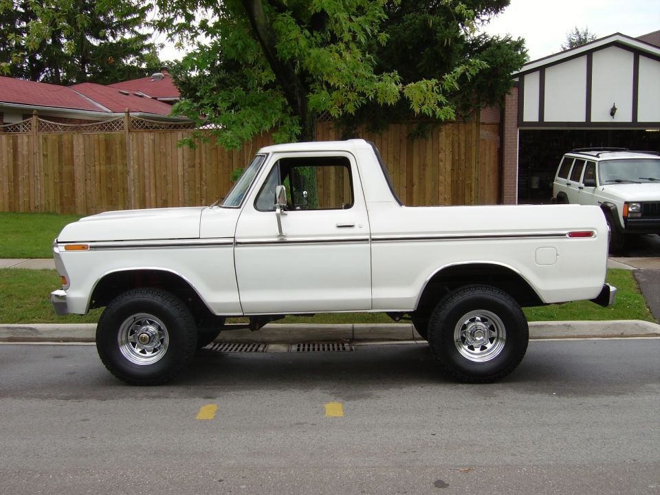 White 1978 Ford Bronco with chrome wheels parked on a street, side view.