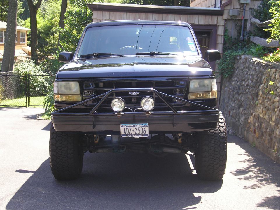 Lifted black Ford Bronco front view with tube bumper, two driving lights and mud tires