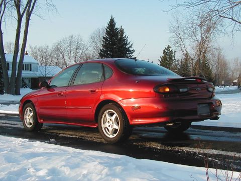 1997 Ford Taurus - A red sedan with a spoiler sits on a snow-covered road under a clear sky.