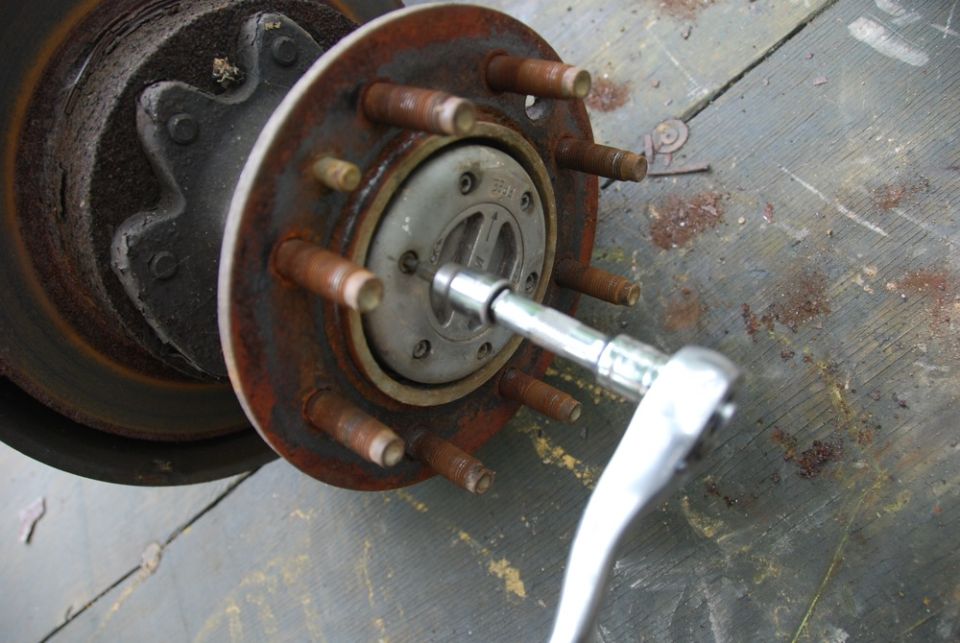 Wheel hub with rusty studs and ratchet wrench on a workbench
