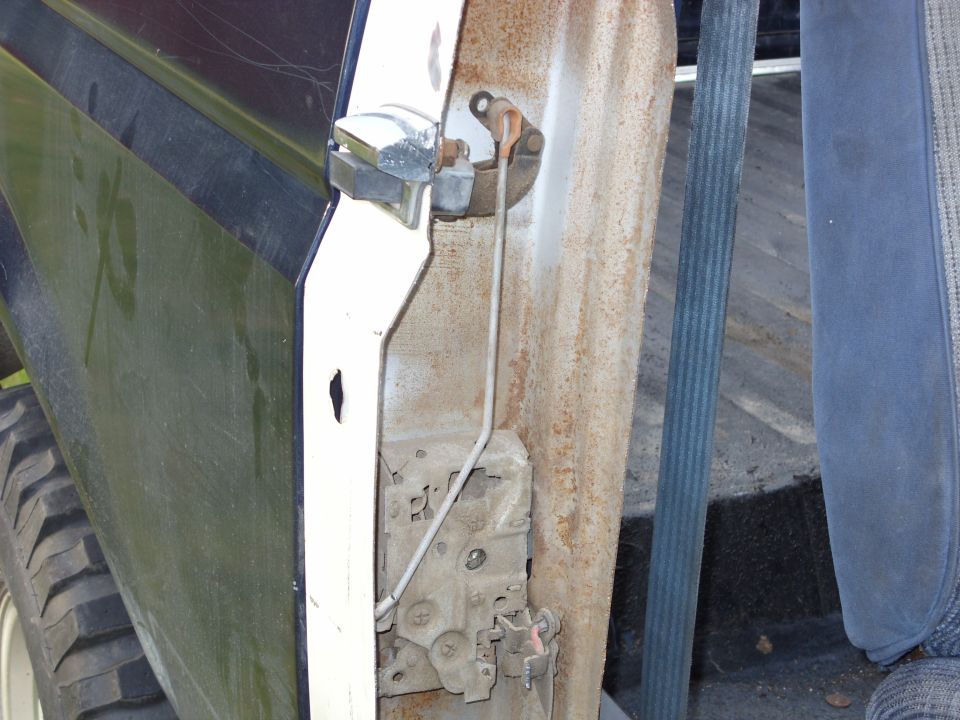 Interior view of a vehicle door latch mechanism with rust and a blue seat.