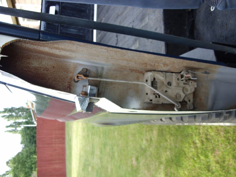 Close-up of a vehicle door interior showing the latch mechanism and rusty metal.