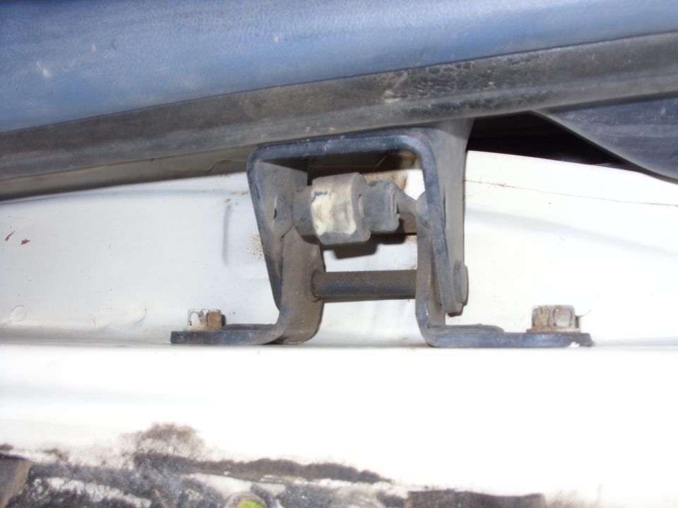 Rusted metal bracket with bolt on white vehicle surface under blue trim