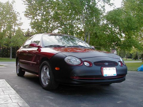 1997 Ford Taurus - This red sedan, identified as a 1997 Ford Taurus, is shown in a 3/4 front view, partially covered by a black car bra.