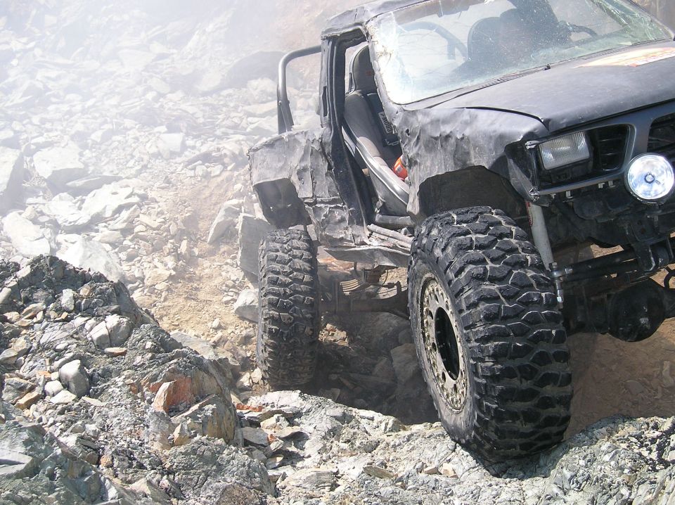 Modified black Toyota Hilux off-roading on a rocky, dusty hill.
