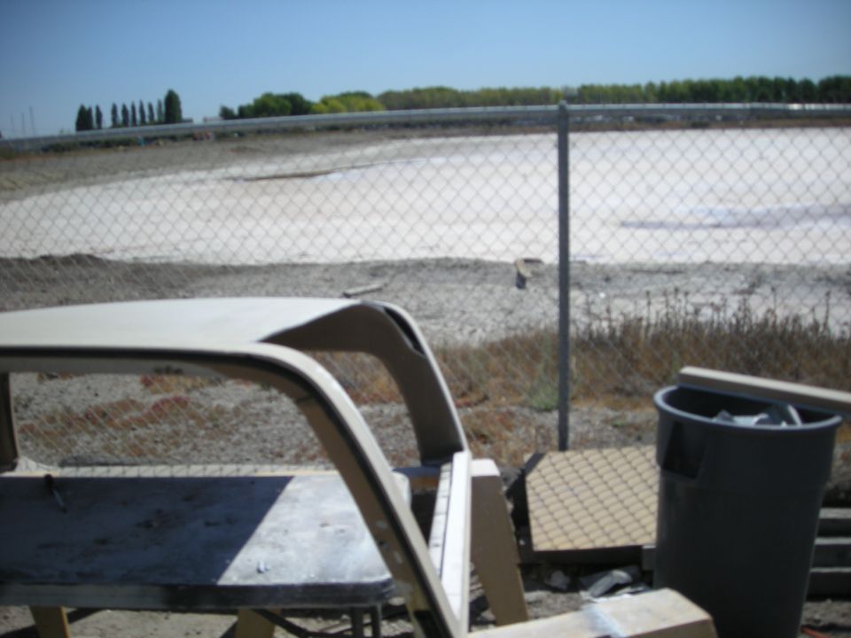 Beige vehicle roof structure in foreground, chain-link fence and dry landscape in background.