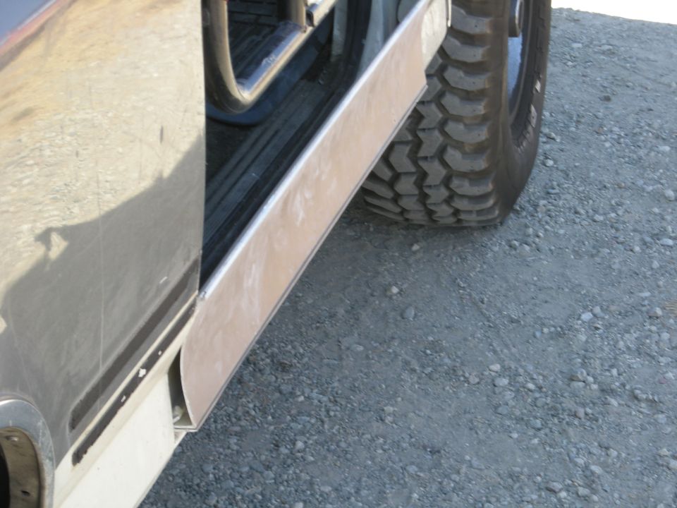Close-up of a vehicle's lower body panel and tire on gravel.