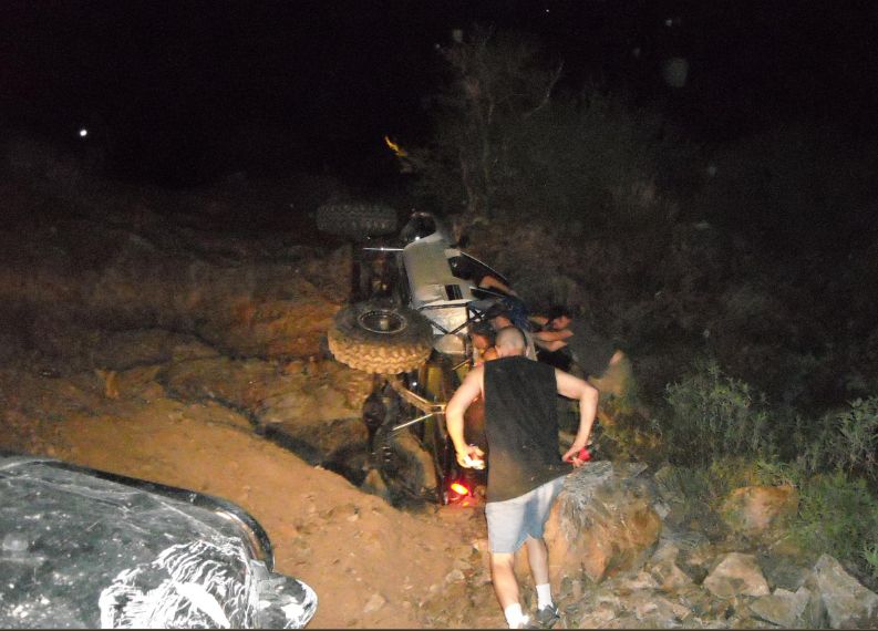 Silver off-road vehicle on its side with people around it at night
