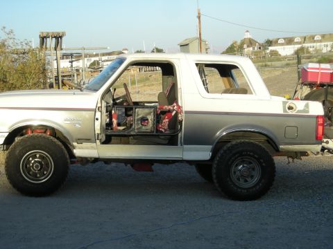 1991 Ford Bronco - This Ford Bronco has its doors removed, revealing a custom interior with a roll cage and patterned seat covers.