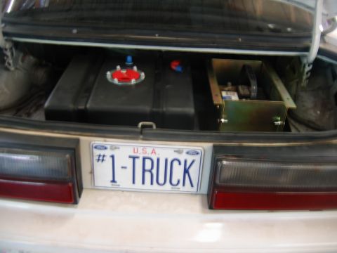 1992 Ford Mustang - Trunk interior with aftermarket fuel cell and battery installation. The license plate says #1-TRUCK.