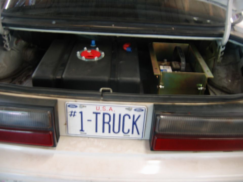 Trunk interior showing a large fuel cell and a battery in a metal box. License plate reads #1-TRUCK