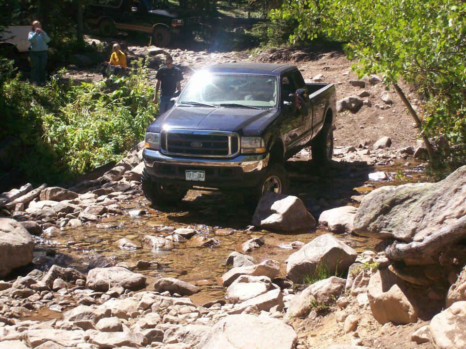 Dark blue Ford pickup truck driving through a rocky stream.
