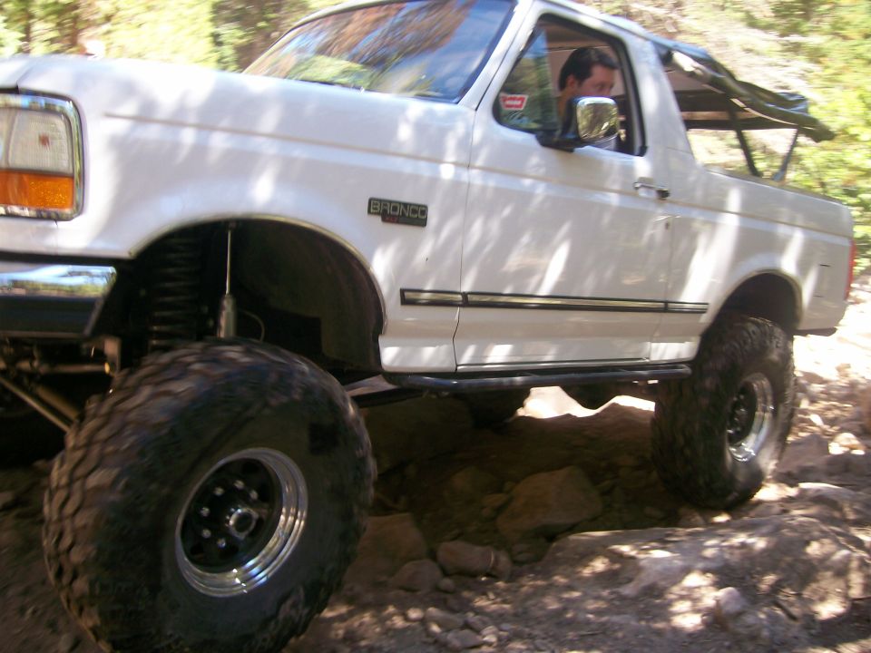 Lifted white Ford Bronco on a rocky off-road trail, front driver's side view.