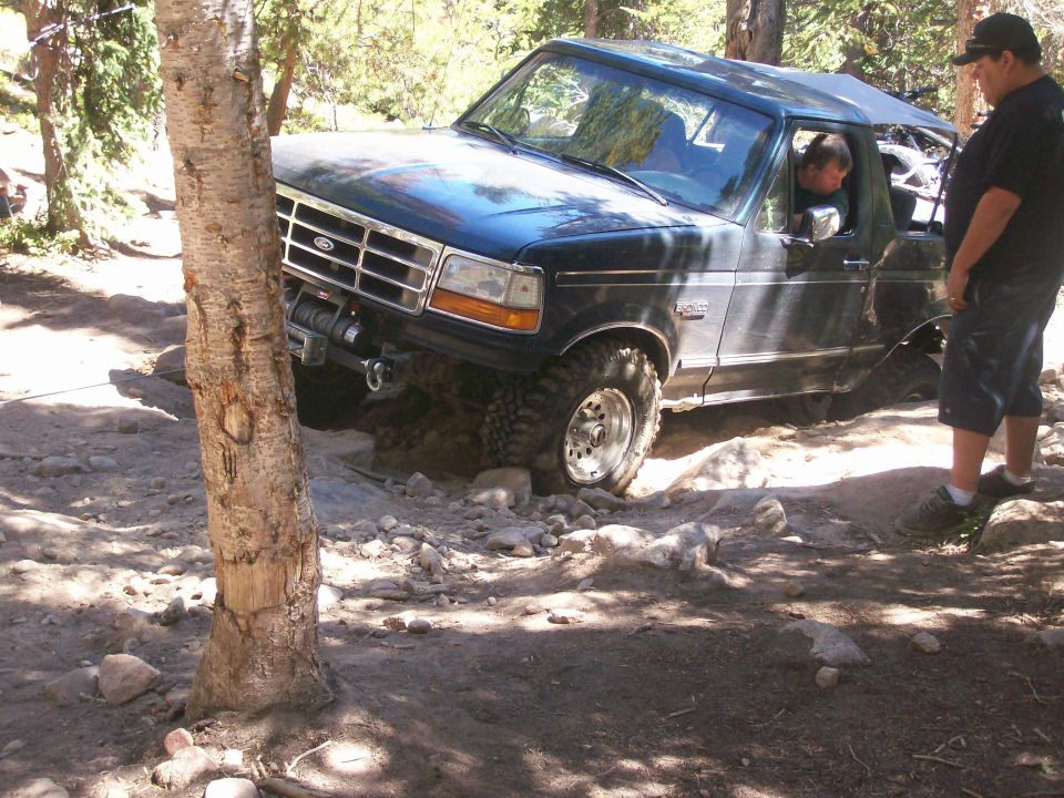 Dark blue Ford Bronco stuck on a rocky trail with a man standing nearby.