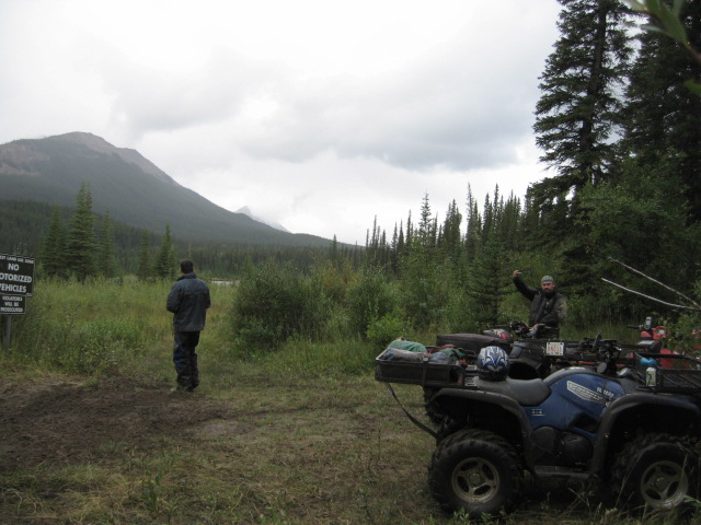 Two men with ATVs in a restricted zone with mountains and trees.