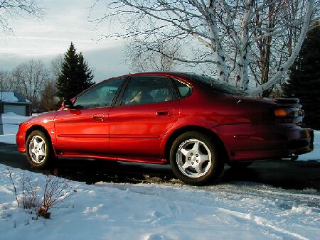 1997 Ford Taurus - This red 1997 Ford Taurus sedan is seen from the side, parked in a snowy environment.