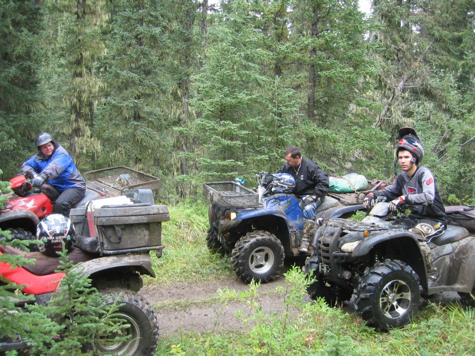 Three ATVs stopped on a muddy forest trail.