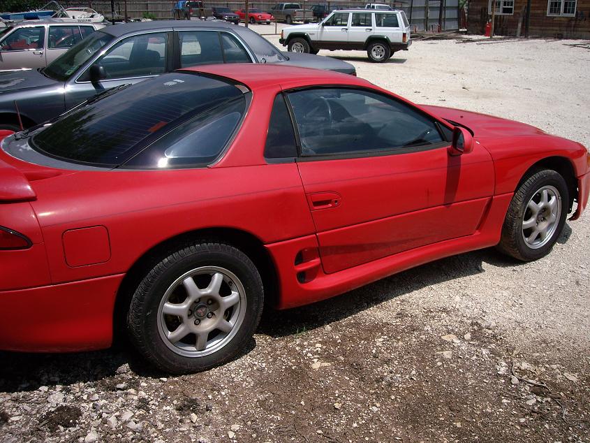 Red Mitsubishi 3000GT parked on a gravel lot, side view.