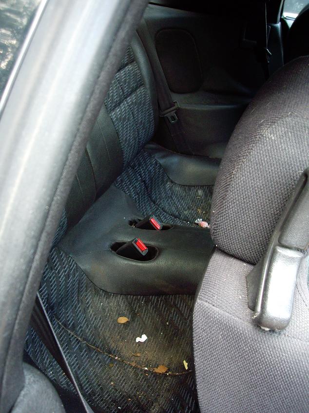 Interior view of a car's rear seats and floor, showing black seats and a dirty floor mat.