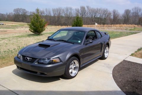 2003 Ford Mustang - A dark gray coupe with a hood scoop and aftermarket wheels is parked on a concrete driveway.