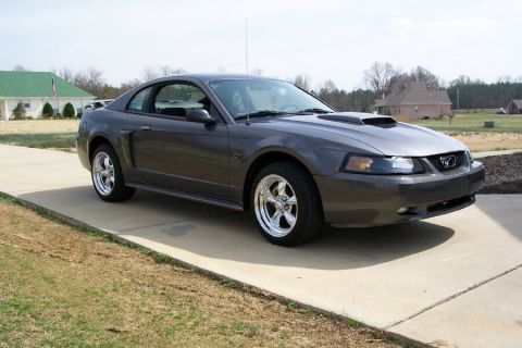 2003 Ford Mustang - This 2003 Ford Mustang coupe features aftermarket chrome wheels and a hood scoop, seen here parked on a driveway.