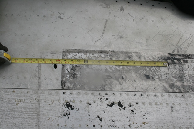 Measuring tape on a damaged, riveted metal surface.
