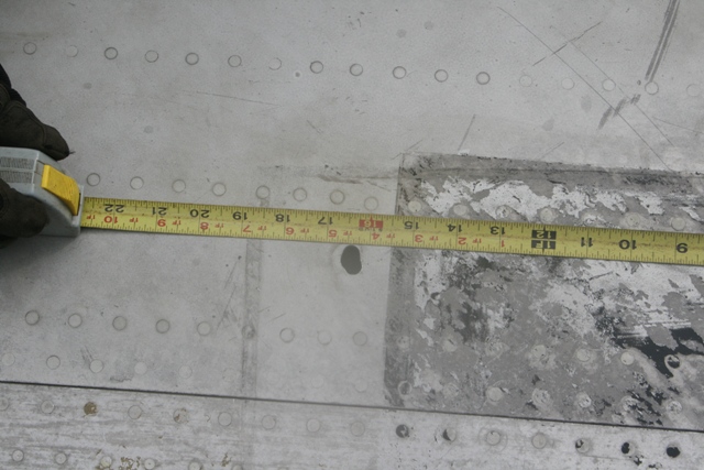 Measuring tape on riveted metal surface showing approximately 15 to 22 inches.