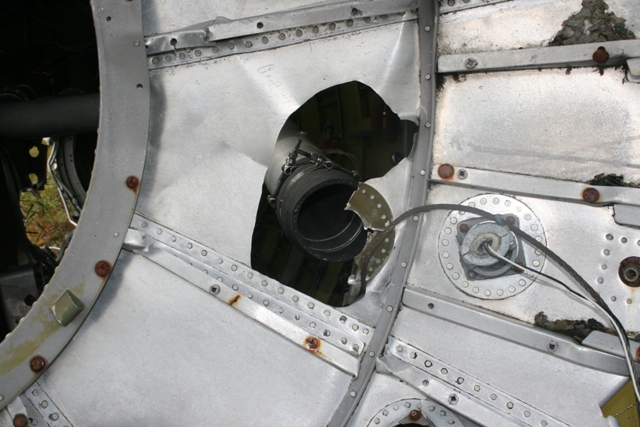 Damaged aluminum airplane fuselage with a large hole and exposed internal components.