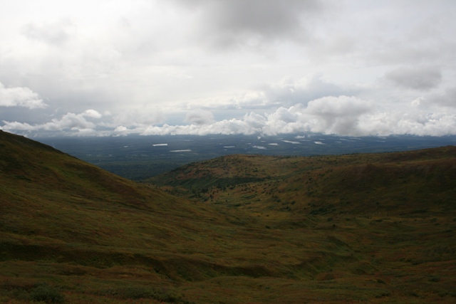 Landscape view of rolling hills and distant lakes under a cloudy sky.