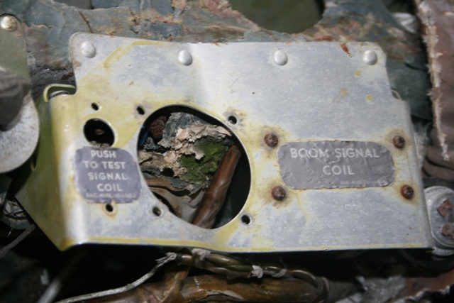 Damaged metal panel with labels "PUSH TO TEST SIGNAL COIL" and "BOOM SIGNAL COIL".