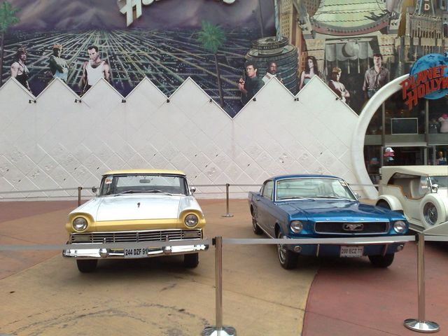 Two classic cars displayed in front of a Planet Hollywood backdrop