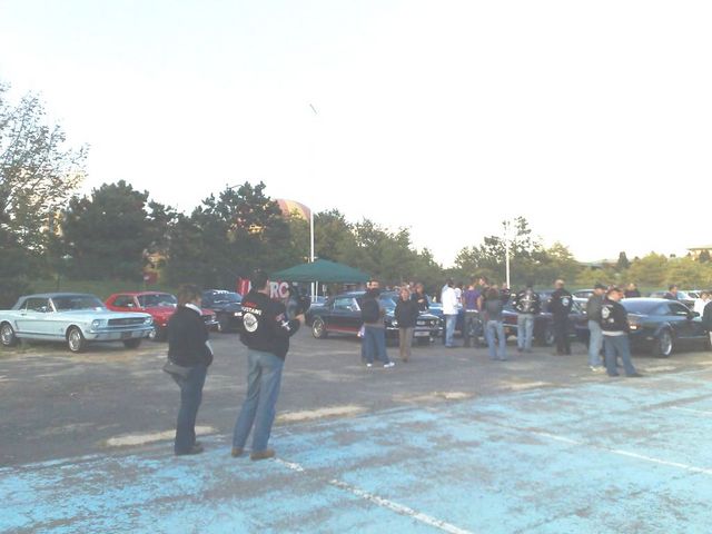 People gathered with classic cars in a parking lot at dusk