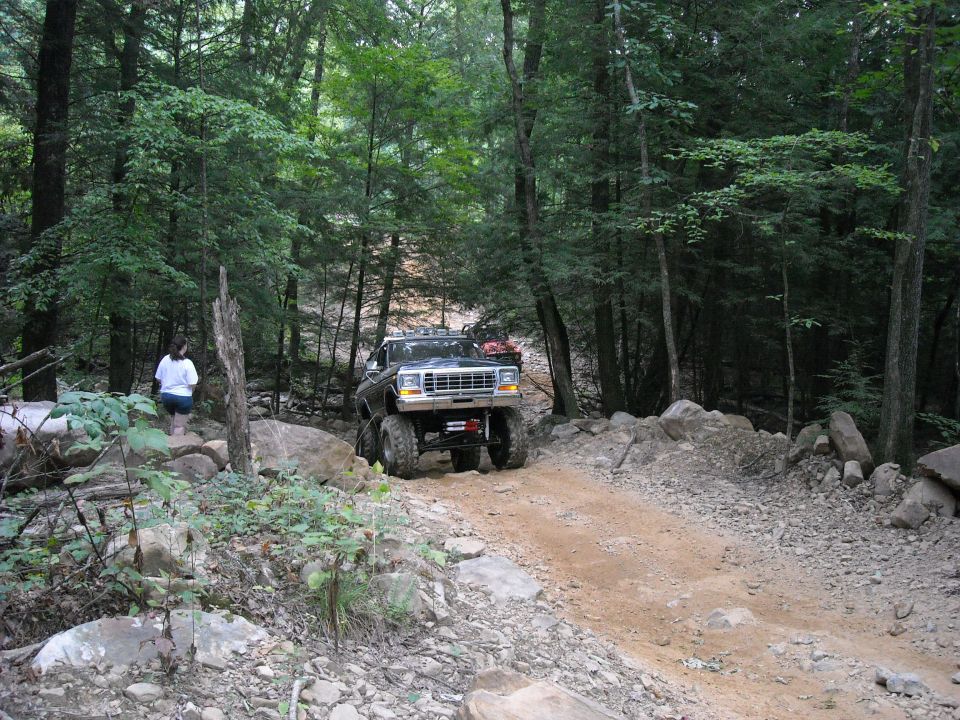 White-fronted lifted truck on a rocky wooded dirt trail with a person nearby