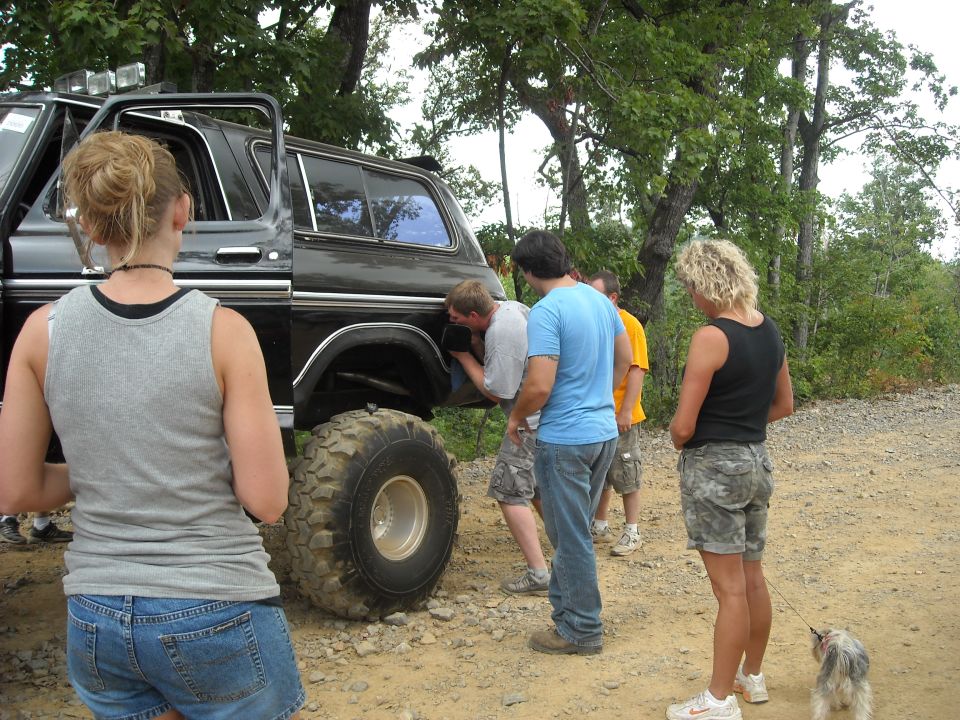 People standing around a black lifted Ford Bronco parked on a dirt trail