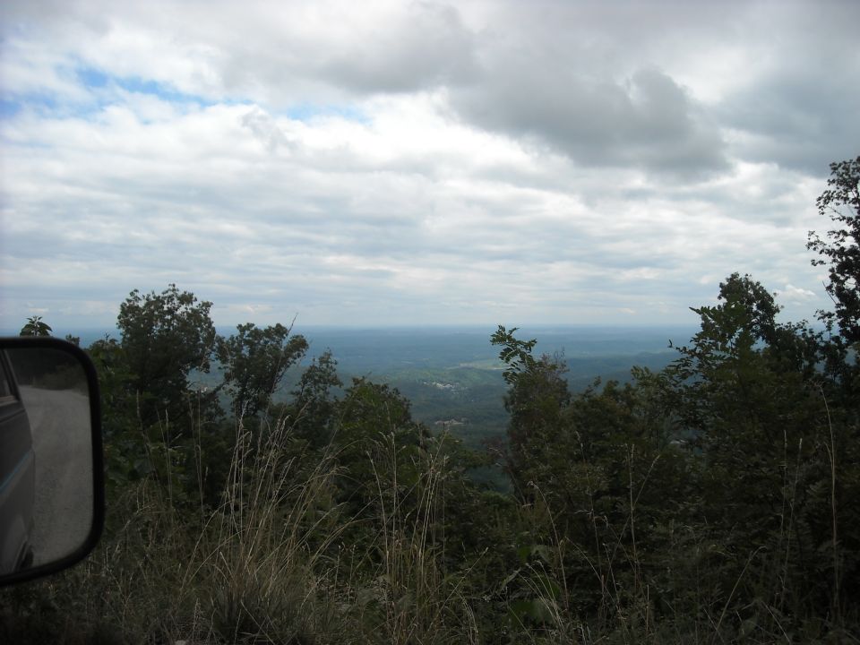Scenic mountain overlook with cloudy sky seen past a vehicle's side mirror