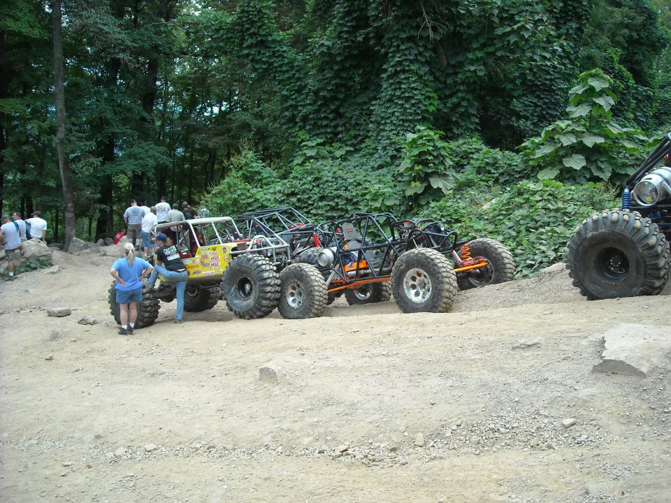 Row of tube-frame rock buggies parked along a dirt trail with spectators