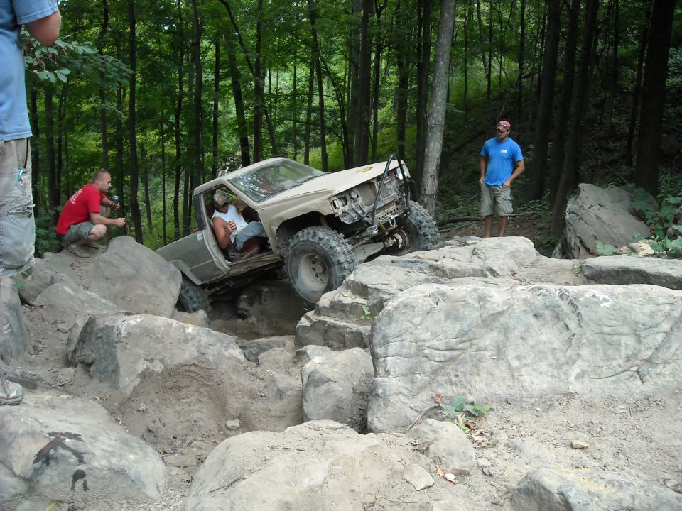 Tan off-road truck climbing boulders at a steep angle in the forest