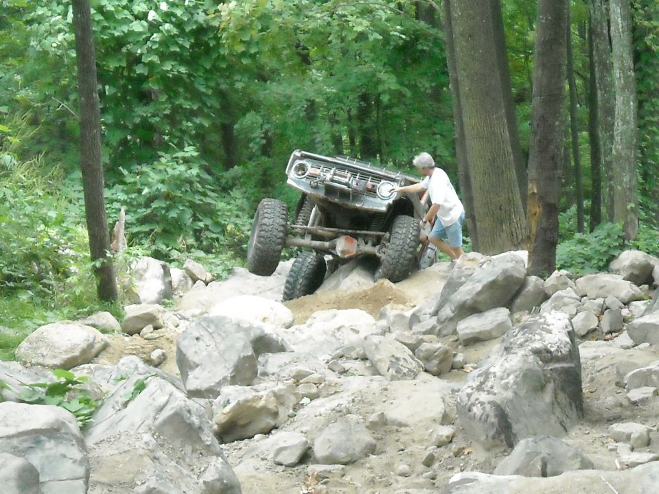 Vintage off-road vehicle crawling boulders with a man spotting in the woods
