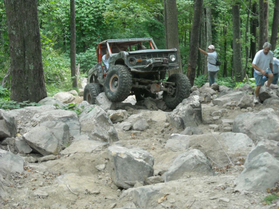 Ford Bronco flexing over rocks with people walking alongside