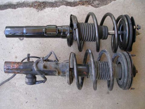 1997 Ford Taurus - Two front strut assemblies laid side by side on a concrete driveway for comparison: the upper unit is freshly painted black with a clean co…