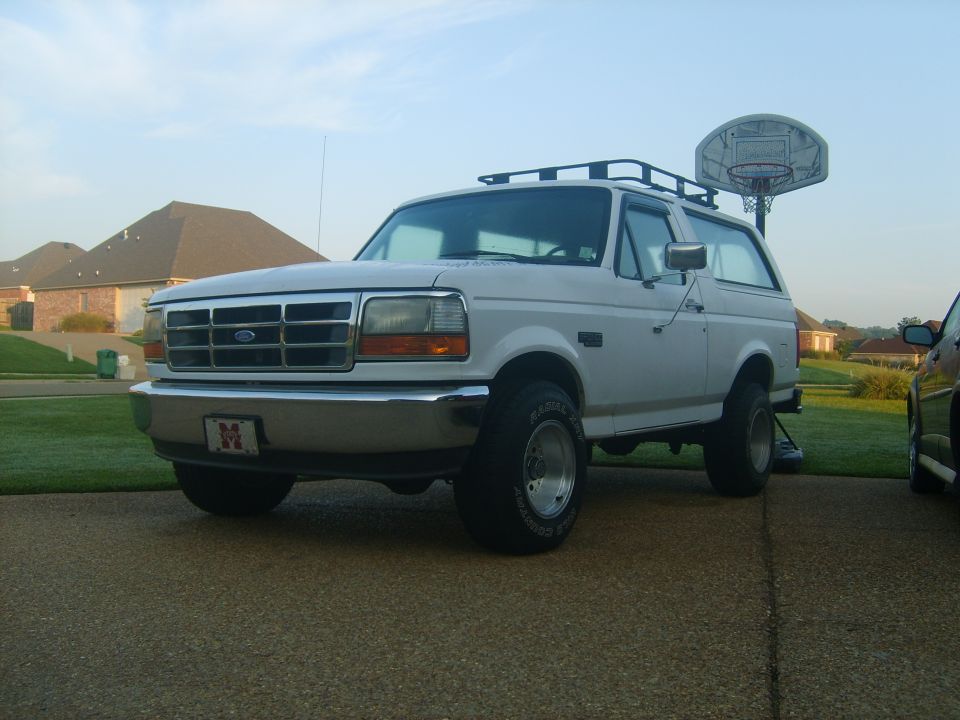 White 1990s Ford Bronco with roof rack parked on a driveway.