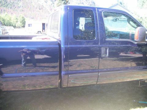 1978 Ford Bronco - The side view of a dark blue pickup truck shows its reflection in the polished paint. A person is visible in the reflection, standing in fr…