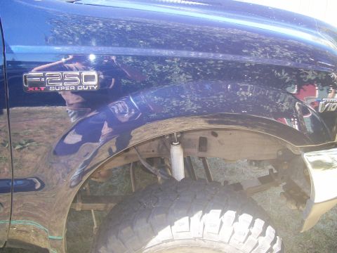 1978 Ford Bronco - A close-up view of the front fender and wheel well of a dark blue Ford F-250 Super Duty pickup truck. The vehicle features a large off-road…