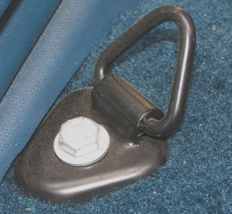 1984 Ford Bronco - A close-up view of a black metal tie-down loop secured to a black metal plate with a silver hex bolt. The loop is attached to a cylindrical…